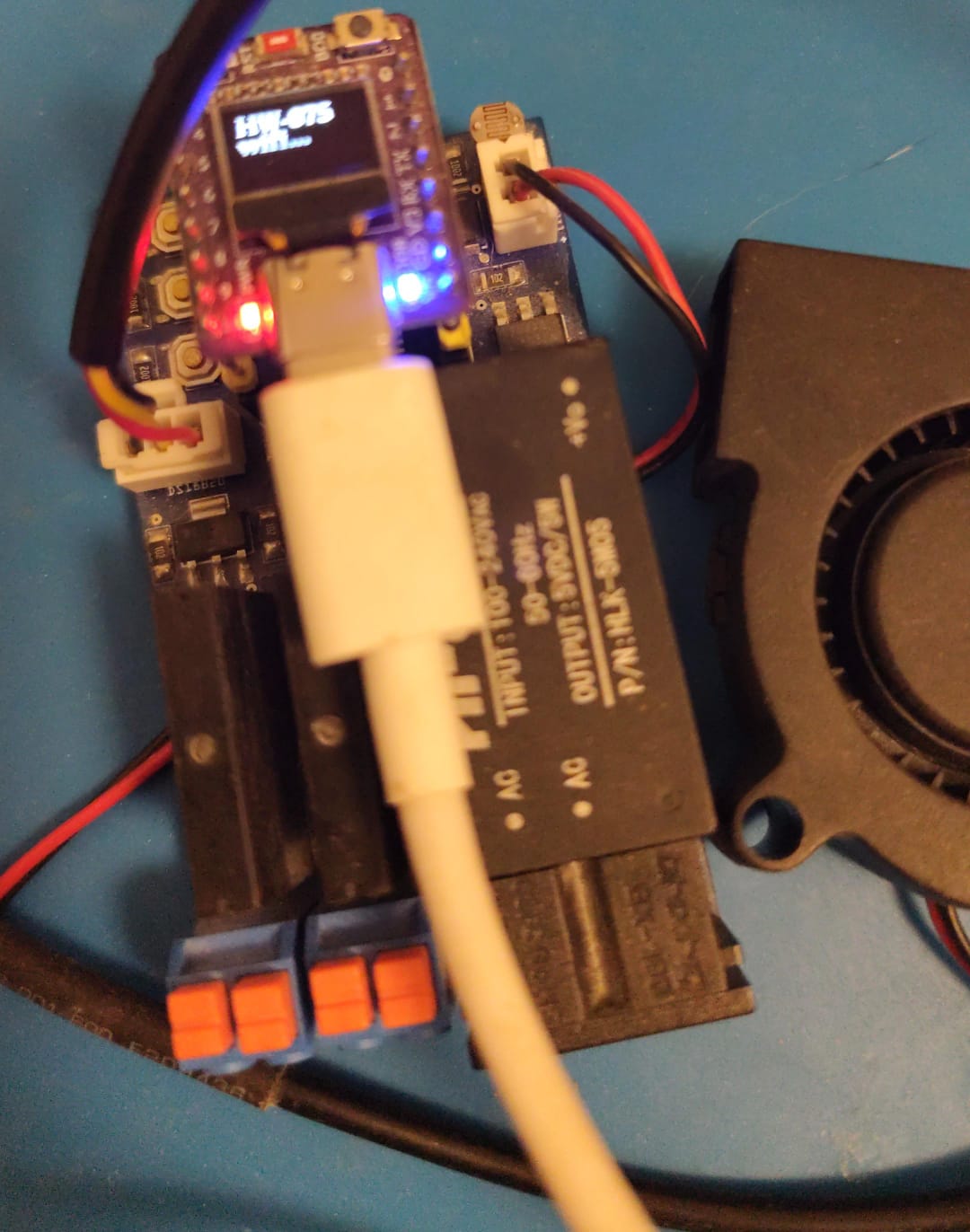Monocontrol, open hardware programmable controller: control board with a display and LEDs, AC-DC power supply, relay module and output terminals, next to a fan